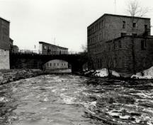 View of the East Mill, showing the four-storey massing and the two-storey adjoining addition, 1972.; Agence Parcs Canada / Parks Canada Agency, 1972.