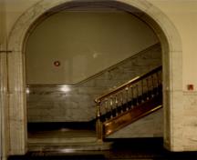 Vue de l'intérieur de l'édifice fédéral, qui montre les couloirs voûtés, entrées, lambris et escaliers en marbre, et les rampes d’escalier en bronze, 1988.; Public Works Canada / Travaux publics Canada, 1988.