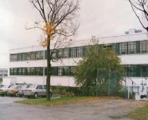 Vue de la façade générale du bâtiment M-12, qui montre la construction en béton armé et le revêtement en stuc blanc des murs extérieurs, 1990.; National Research Council Canada / Conseil national de recherches du Canada, 1990.