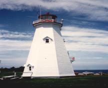 Vue de l'extérieur de la tour, qui montre la lanterne en acier peint en rouge proportionnée à la tour et le garde-fou caractéristique à croisillons en bois, 1990.; Transport Canada / Transports Canada, 1990.