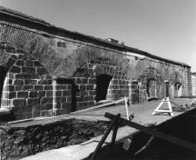 Vue de la façade du bâtiment 21, qui montre les six grands arcs surbaissés soutenus par des pilastres, chaque ouverture étant surmontée d’un arc en pierre, vers 1980.; Department of National Defence / Ministère de la Défense nationale, circa 1980.