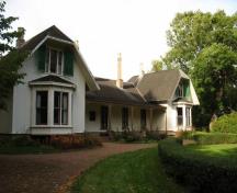 General view of Ardgowan House, showing the Gothic Revival style features such as the shingled hipped gable roof with prominent projecting chimneys and the verandah fretwork.; Parks Canada Agency / Agence Parcs Canada.