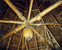 Vue de l'intérieur du pavillon Dévonien, qui montre le toit exposé et le motif en gland taillé à l’extrémité de la poutre centrale, 1997.; Agence Parcs Canada / Parks Canada Agency, 1997.