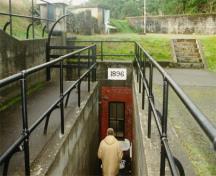 Vue de l'entrée principale du dépôt de munitions de la batterie supérieure, montrant les marches qui se rendent à l'entrée, protégées par des balustrades de pipes. La fenêtre de l'abri de l'équipage est également représenté sur la photo, 1997.; Agence Parcs Canada / Parks Canada Agency, J. Mattie, 1997.