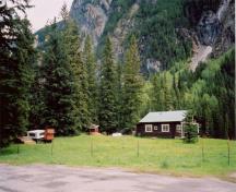 Panoramic view of Ranch-cabin and surroundings from the south driveway demonstrating its scenic location in the Yoho Valley, adjacent to flat pasture land on one side and a tall stand of coniferous trees on the other, 1999.; Cultural Resource Services, Calgary/Ressources culturelles, Calgary, 1999.