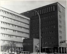 Corner view of the Surveys and Mapping Building, showing the recessed bands of windows with continuous stone sills, and continuous bands of stone above the windows forming ‘brise-soleil’ at each storey, 1994.; Parks Canada Agency / Agence Parcs Canada, 1994.
