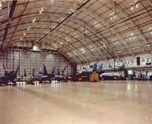 Interior view of Hangar 3 showing the long span, three-hinged segmented steel truss arches which frame the bowed roof and create a large, austere, column-free space and suitable for the storage and maintenance of aircrafts, 1999.; Department of National Defence / Ministère de la Défense nationale, 1999.