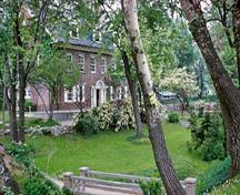 Panoramic view of the Hough House emphasizing its domestic scale, Colonial Revival style, and stone and wood materials which harmonize with its park-like landscape at the National Historic Site, 1960.; Parks Canada Agency / Agence Parcs Canada, 1960.