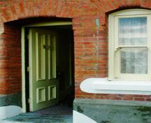 Detail view of the main entrance to the Warrant Officer's Quarters emphasizing the red brick walls and the continuous projecting base, just below sill height, 1997.; Parks Canada Agency / Agence Parcs Canada, J. Mattie, 1997.