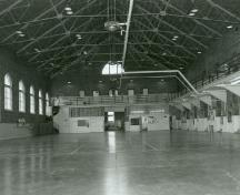 Interior view of the Armoury, showing the large unobstructed drill hall with exposed iron Fink truss system, 1990.; Department of National Defence / Ministère de la Défense nationale, 1990.