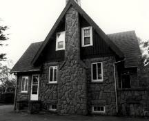 Side view of the Superintendent's Residence, showing the steeply pitched, shingled, gable roof with a stone chimney, c. 1990.; Parks Canada Agency / Agence Parcs Canada, c./v. 1990.