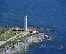 General view of Cap-des-Rosiers lighthouse, showing its rugged, exposed site atop high cliffs on a point of land separating two major bodies of water.; Parks Canada Agency / Agence Parcs Canada.