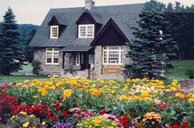 Façade du centre d’information aux visiteurs Est, qui montre le porche d’entrée central créé par le prolongement du toit par-dessus l’entrée, la façade avant à trois baies et le prolongement du mur pignon à l’avant, 1987.; Parks Canada Agency / Agence Parcs Canada, 1987.