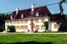 General view of Mauvide-Genest Manor, showing the substantial two-storey rectangular massing of the manor’s main block under a steeply hipped roof broken by small dormer windows and two large chimneys.; Parks Canada Agency / Agence Parcs Canada.