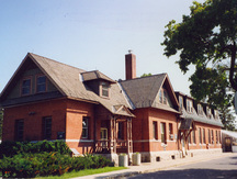 View of the exterior of the Cereal Crops Building, showing the composition and detailing of the front porch, in particular, the turned posts, 1995.; Parks Canada Agency / Agence Parcs Canada, 1995.