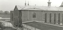 View of the Main Cellblock's north wing, showing the exterior stonework and tall arched windows, 1990.; Parks Canada Agency / Agence Parcs Canada, 1990.