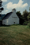 Vue de l'arrière de la maison des Français, qui montre le toit à deux versants très pentu et l’imposante cheminée avec le four à bois extérieur intégré, 1991.; Parks Canada Agency / Agence Parcs Canada, Christine Chartré, 1991.