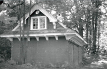 View of the façade of the Wood Shed, showing the gable roof with overhanging and flared eaves supported by large brackets, 1984.; Parks Canada | Parcs Canada, Robert Hunter, 1984.