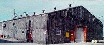 Vue générale de l'Édifice de l'aérogare, montrant son revêtement extérieur de panneaux métalliques nervurés préfabriqués et la taille, la forme et l’espacement des ouvertures de la porte et des fenêtres, 1998.; North Warning System Office / Bureau du système d'alerte du Nord, 1998.